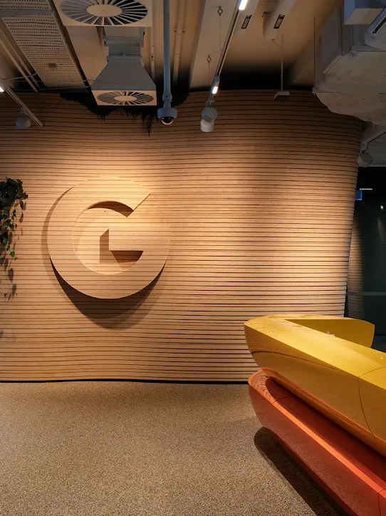 Un lobby de oficina con el logotipo de Google, un mostrador de recepción y diversas plantas.